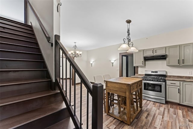 kitchen with stainless steel gas range oven, dark wood-type flooring, hanging light fixtures, gray cabinets, and a notable chandelier