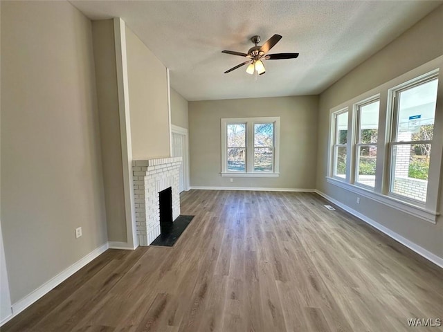 unfurnished living room with ceiling fan, a textured ceiling, a fireplace, and light hardwood / wood-style floors