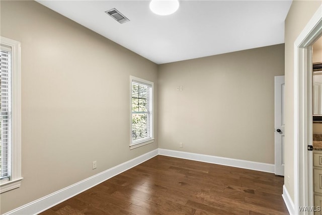 empty room featuring baseboards, dark wood-style floors, and visible vents
