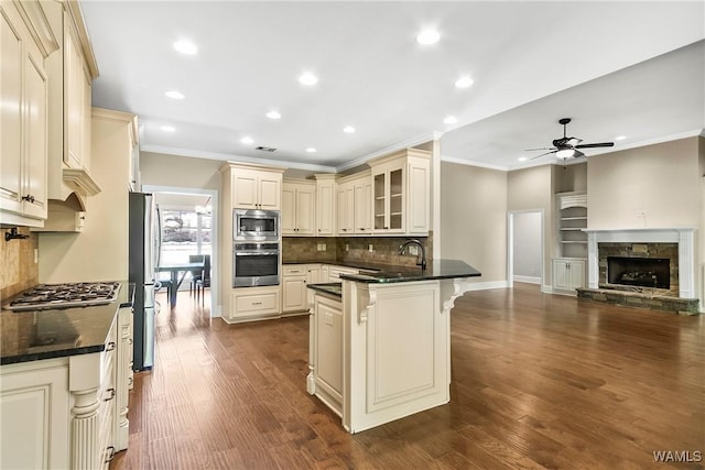 kitchen featuring ceiling fan, ornamental molding, stainless steel appliances, open floor plan, and cream cabinets