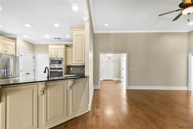 kitchen featuring baseboards, cream cabinets, crown molding, and appliances with stainless steel finishes