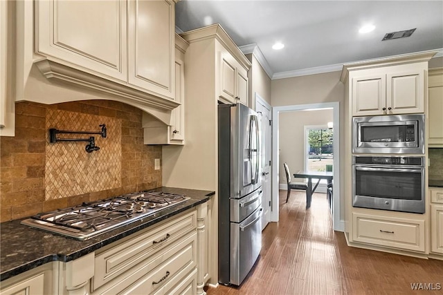 kitchen with tasteful backsplash, ornamental molding, visible vents, and stainless steel appliances