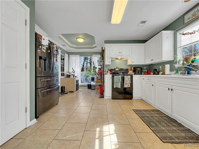 kitchen with a raised ceiling, stainless steel refrigerator with ice dispenser, light tile patterned flooring, black electric range oven, and white cabinets