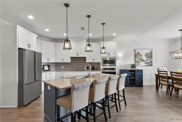 kitchen with appliances with stainless steel finishes, white cabinetry, sink, decorative light fixtures, and a center island with sink