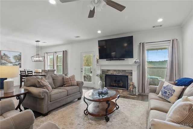 living room featuring ceiling fan with notable chandelier, light hardwood / wood-style flooring, a fireplace, and crown molding