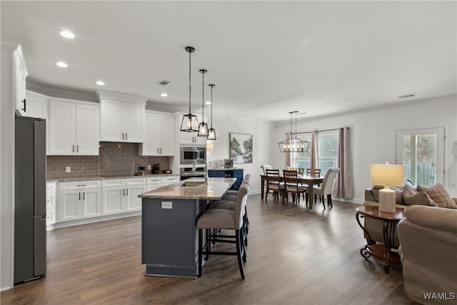 kitchen featuring white cabinets, appliances with stainless steel finishes, decorative light fixtures, sink, and a center island with sink