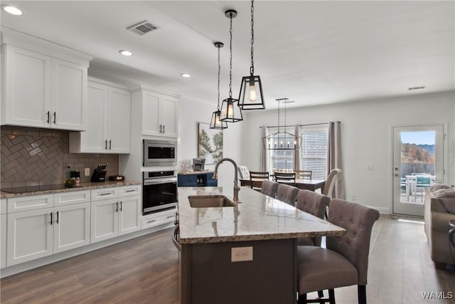 kitchen featuring white cabinets, appliances with stainless steel finishes, decorative light fixtures, a kitchen island with sink, and a breakfast bar area