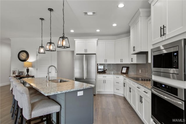 kitchen featuring sink, stainless steel appliances, white cabinetry, and an island with sink