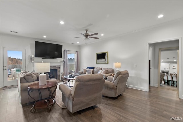 living room with hardwood / wood-style flooring, a stone fireplace, ceiling fan, and ornamental molding