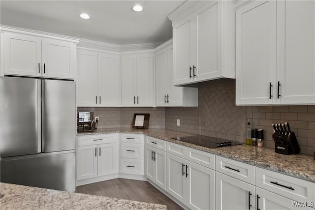 kitchen featuring tasteful backsplash, white cabinetry, light stone counters, black electric cooktop, and stainless steel refrigerator