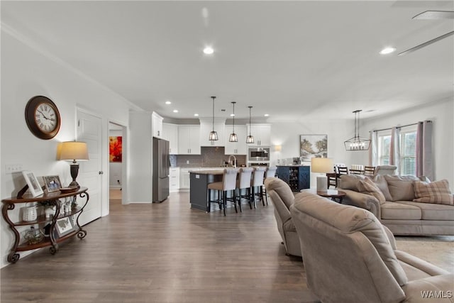 living room featuring sink, crown molding, dark wood-type flooring, and an inviting chandelier