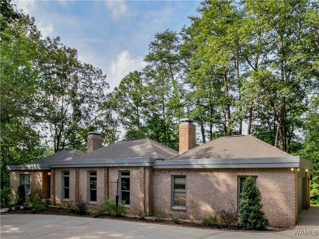 view of front of property with a shingled roof, brick siding, and a chimney