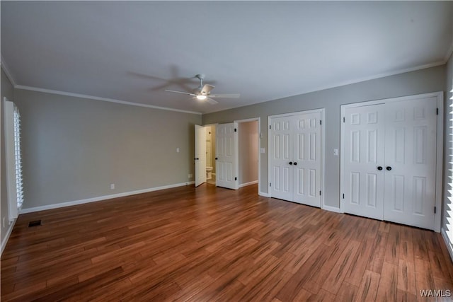 unfurnished bedroom with ceiling fan, baseboards, multiple closets, ornamental molding, and wood finished floors