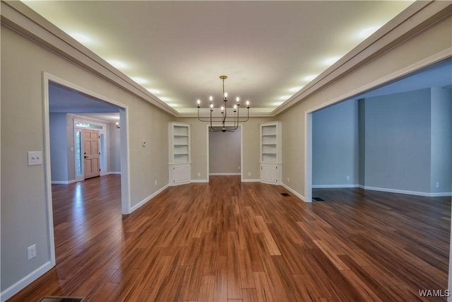 empty room featuring built in features, dark wood-style floors, baseboards, a tray ceiling, and a notable chandelier