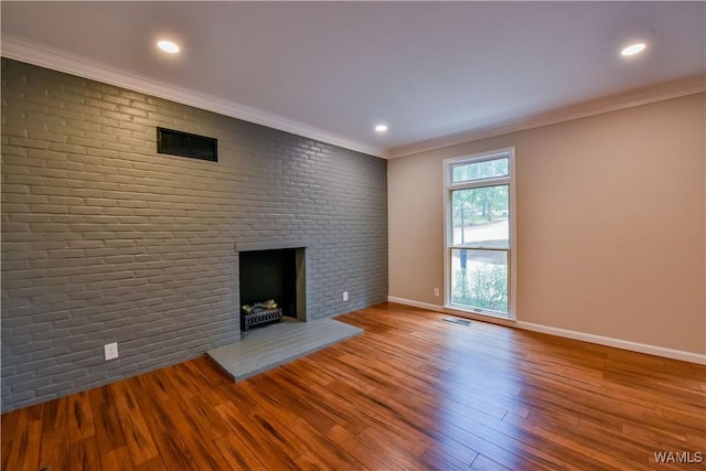 unfurnished living room with visible vents, wood finished floors, brick wall, crown molding, and a brick fireplace