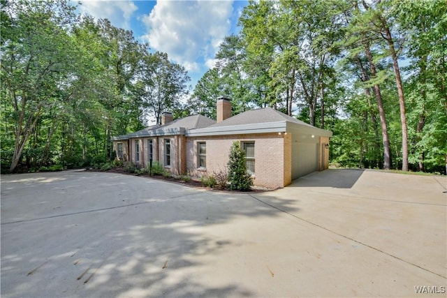 view of home's exterior featuring brick siding, driveway, a chimney, and an attached garage