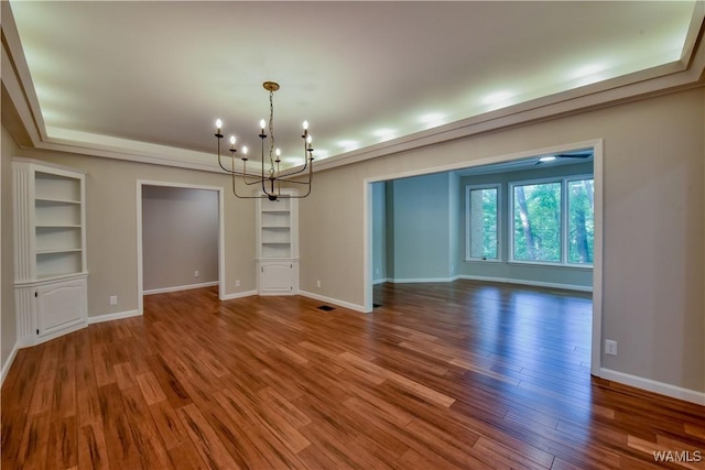 empty room with an inviting chandelier, built in shelves, wood finished floors, and baseboards