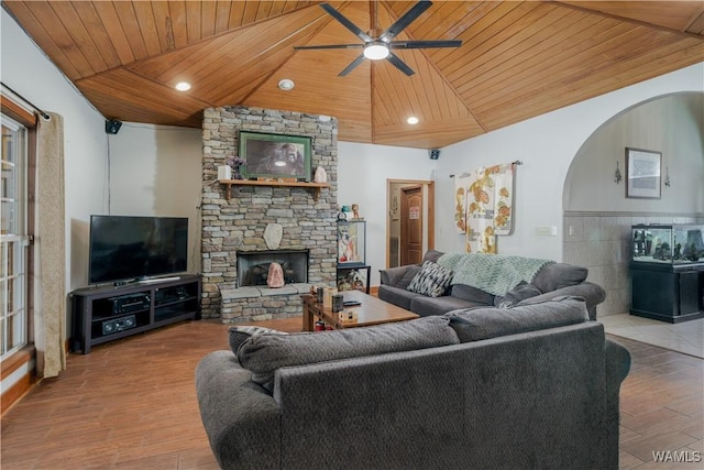 living room with ceiling fan, a stone fireplace, wood ceiling, light hardwood / wood-style floors, and lofted ceiling