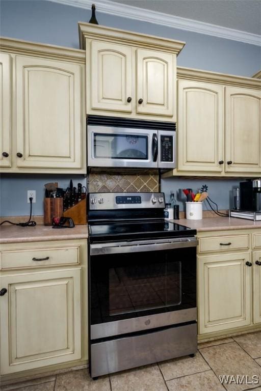 kitchen with light countertops, crown molding, cream cabinetry, and stainless steel appliances