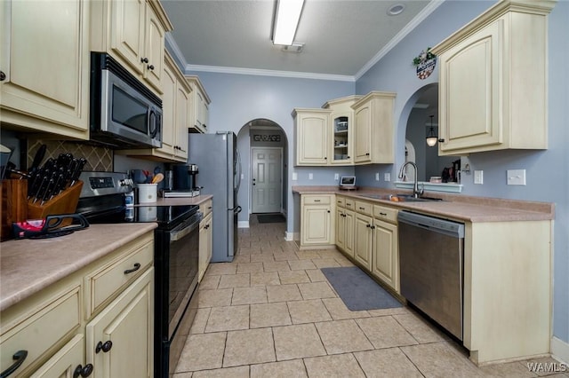 kitchen featuring arched walkways, appliances with stainless steel finishes, cream cabinetry, and a sink