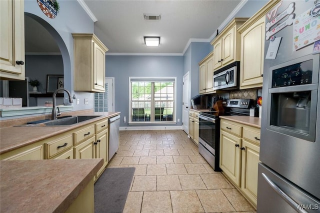 kitchen with a sink, tasteful backsplash, crown molding, appliances with stainless steel finishes, and cream cabinets