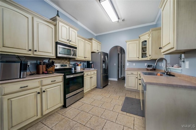kitchen featuring crown molding, a sink, cream cabinets, arched walkways, and appliances with stainless steel finishes