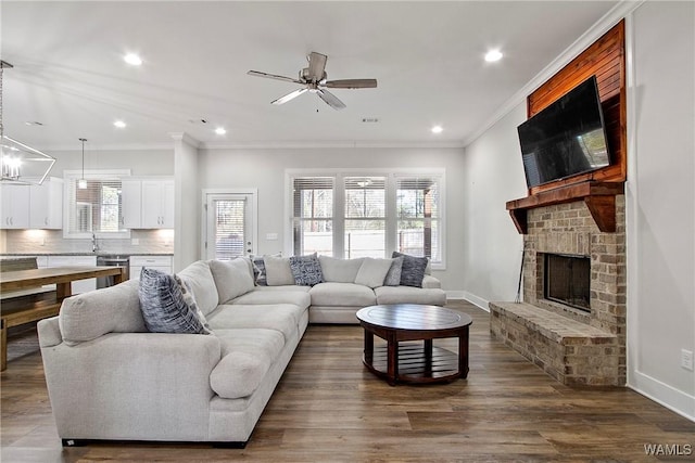 living room featuring dark wood-style floors, baseboards, recessed lighting, crown molding, and a brick fireplace