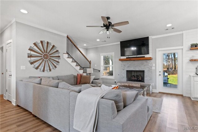 living area featuring a stone fireplace, wood finished floors, visible vents, and crown molding