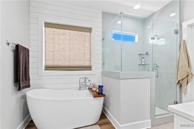 bathroom featuring a stall shower, wood walls, wood finished floors, a freestanding tub, and baseboards