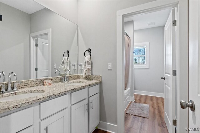 full bathroom featuring double vanity, baseboards, a sink, and wood finished floors