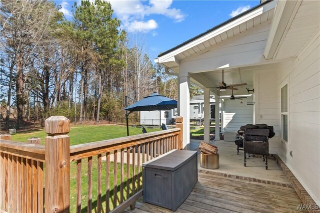 wooden terrace with fence, a ceiling fan, and a lawn