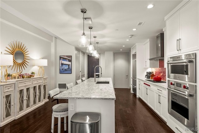 kitchen featuring double oven, white cabinets, a sink, and wall chimney exhaust hood