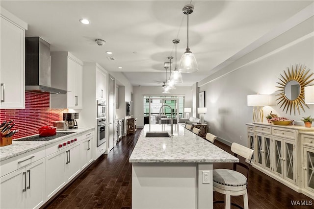 kitchen with white gas stovetop, wall chimney exhaust hood, open floor plan, hanging light fixtures, and white cabinetry