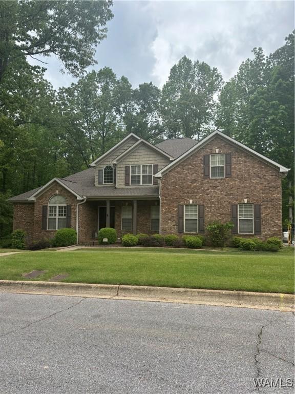 view of front of house featuring a front yard, a shingled roof, and brick siding