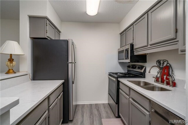 kitchen featuring sink, gray cabinets, light wood-type flooring, a textured ceiling, and stainless steel appliances