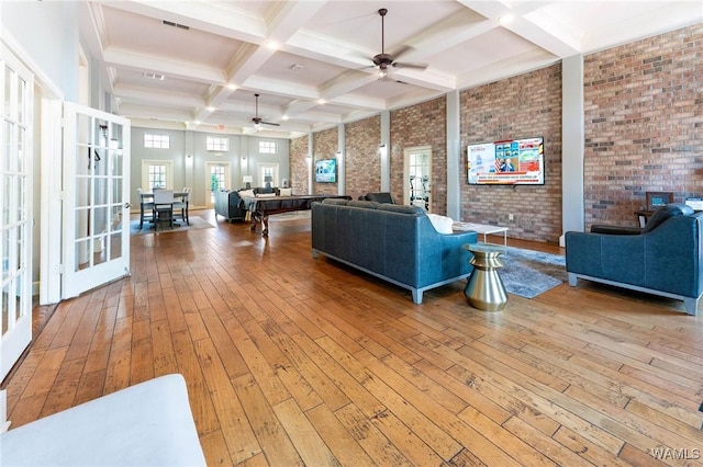 living area featuring coffered ceiling, beamed ceiling, brick wall, ceiling fan, and hardwood / wood-style flooring