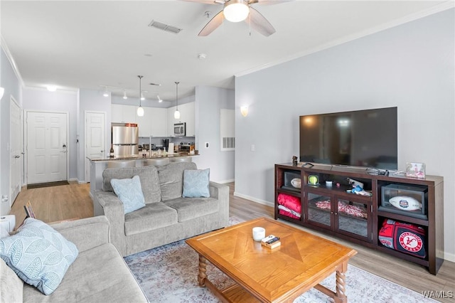 living room featuring ornamental molding, visible vents, light wood-style floors, and ceiling fan