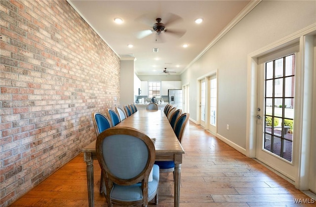 dining space featuring light wood-type flooring, baseboards, brick wall, a ceiling fan, and ornamental molding
