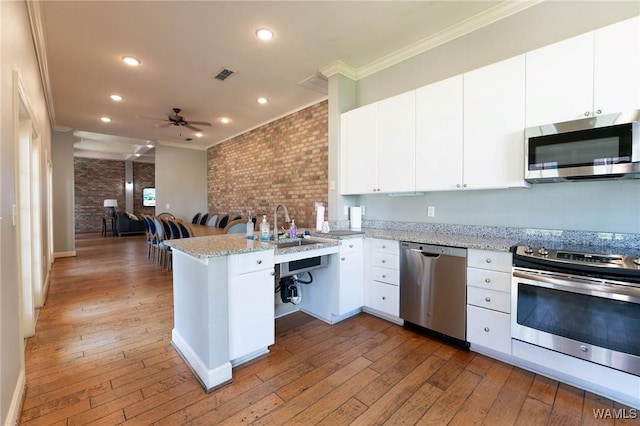 kitchen featuring a peninsula, visible vents, a ceiling fan, appliances with stainless steel finishes, and ornamental molding