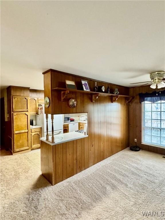 kitchen with ceiling fan, kitchen peninsula, white fridge, light colored carpet, and wooden walls