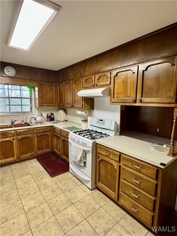 kitchen with light tile patterned floors, sink, and white range with gas cooktop