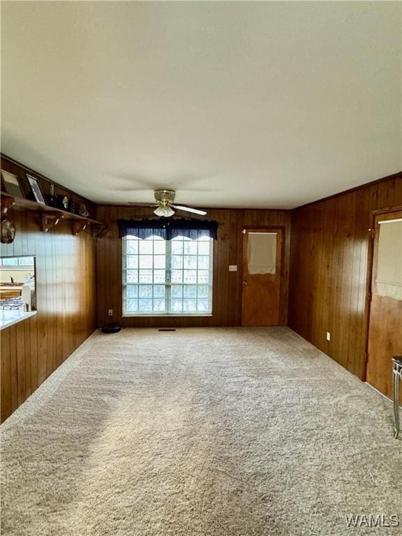 empty room with ceiling fan, wooden walls, and carpet