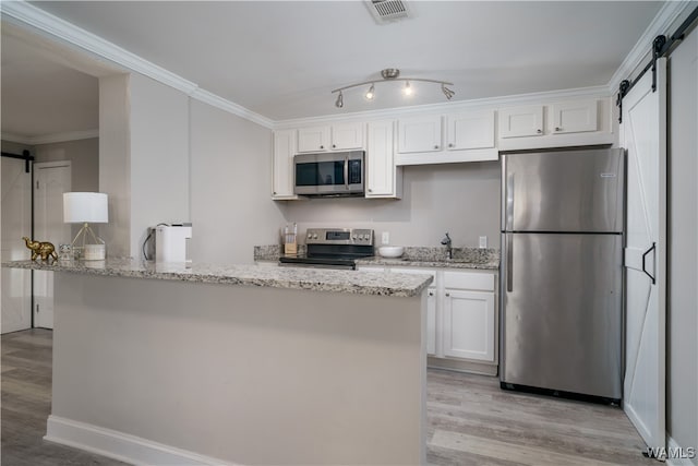 kitchen with light stone countertops, stainless steel appliances, a barn door, and white cabinets