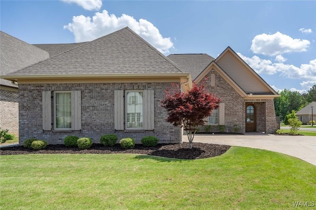 view of front of property featuring roof with shingles, concrete driveway, a front yard, and brick siding