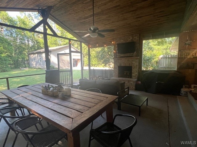 sunroom / solarium featuring an outdoor stone fireplace, ceiling fan, and vaulted ceiling