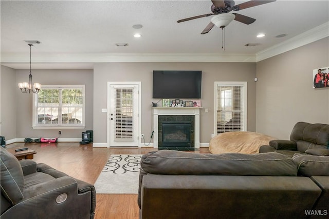 living room featuring baseboards, a premium fireplace, wood finished floors, crown molding, and ceiling fan with notable chandelier