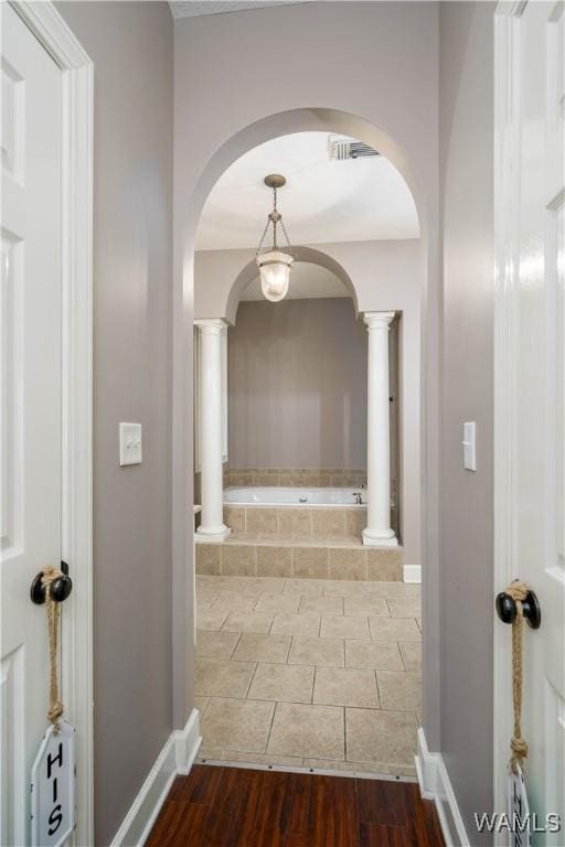 corridor featuring ornate columns, visible vents, baseboards, and wood finished floors