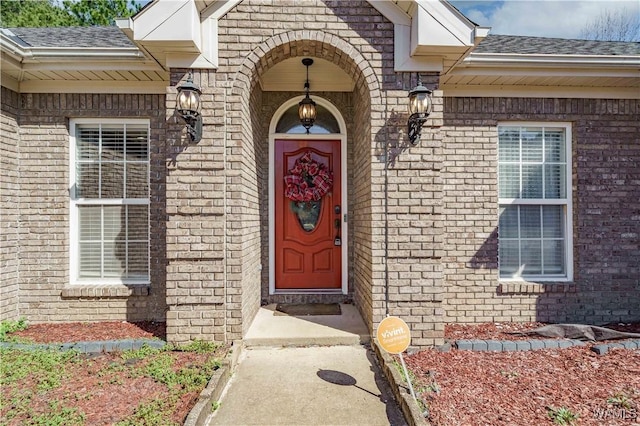 doorway to property with roof with shingles and brick siding