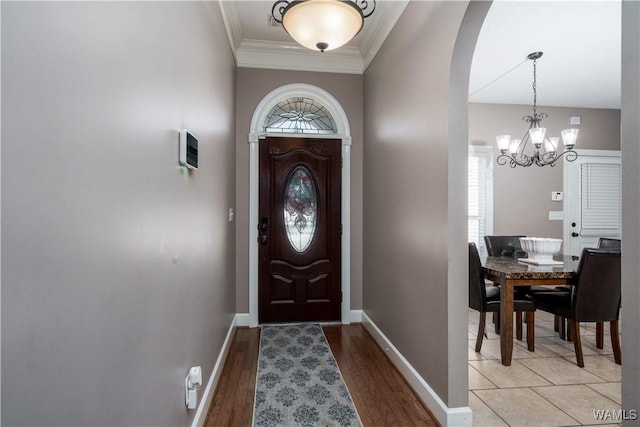 entryway featuring arched walkways, a chandelier, light wood-style flooring, baseboards, and ornamental molding