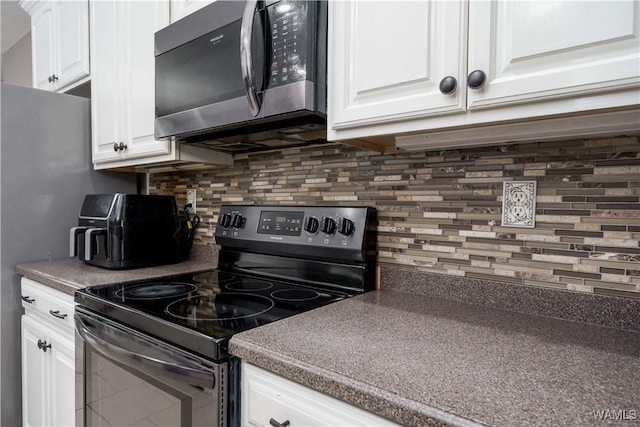 kitchen featuring white cabinetry, black electric range oven, tasteful backsplash, stainless steel microwave, and dark countertops